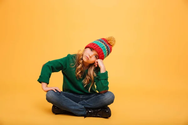 Znuděná holka v svetr a čepice sedí na podlaze — Stock fotografie