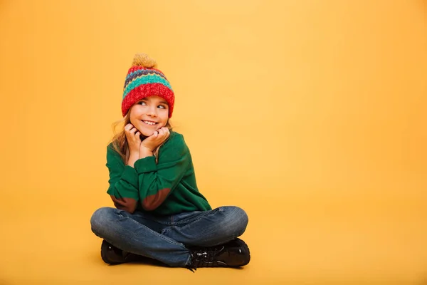 Девочка в свитере и шляпе сидит на полу — стоковое фото
