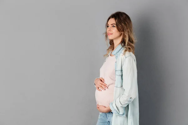 Vista lateral de una mujer embarazada sonriente sosteniendo su barriga — Foto de Stock
