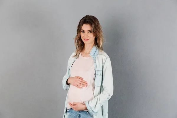 Mujer embarazada sonriente sosteniendo su barriga y mirando a la cámara — Foto de Stock