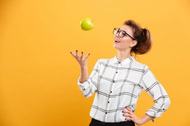 Portrait of healthy woman in plaid shirt throwing green apple up