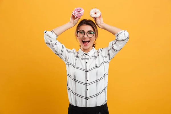 Портрет позитивной женщины в клетчатой рубашке с двумя вкусными пончиками — стоковое фото