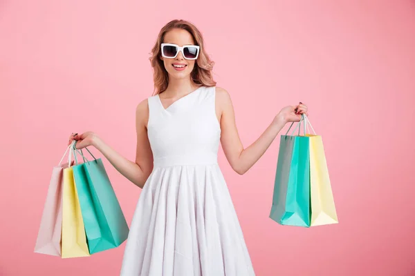 Boldog, fiatal nő, fárasztó napszemüveg gazdaság bevásárló táskák. — Stock Fotó