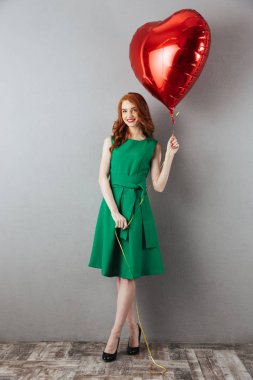 Kalp balon tutan Kızıl saçlı genç gülümseyen.