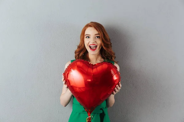 Surprised redhead young woman holding heart balloon. — Stock Photo, Image