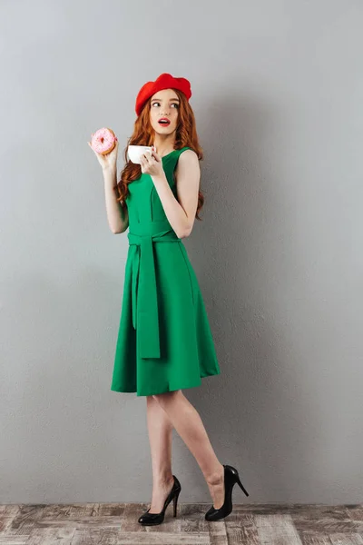Redhead young cute lady eating donut and drinking coffee. — Stock Photo, Image