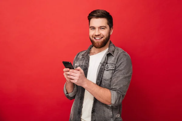 Sorrindo barbudo homem segurando smartphone e olhando para a câmera — Fotografia de Stock