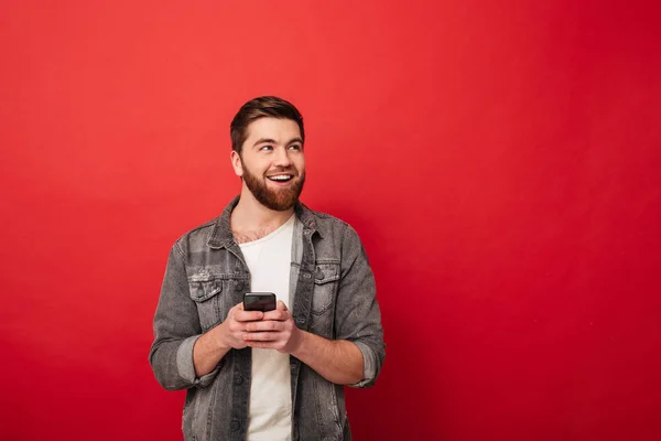 Образ щасливого бородатого чоловіка тримає смартфон і дивиться вбік — стокове фото