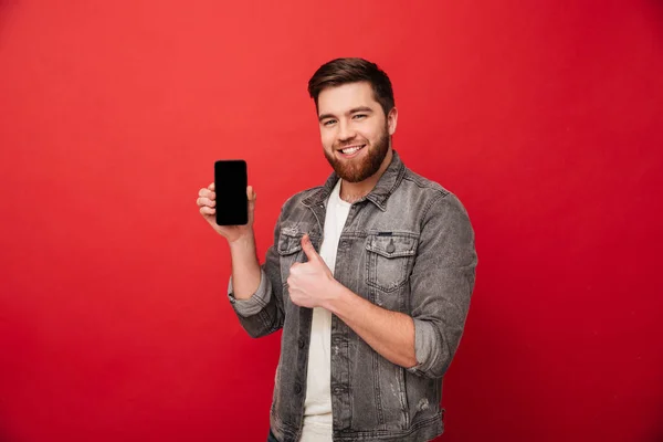 Bilden av orakad lycklig man i denim presentera mobiltelefon på — Stockfoto