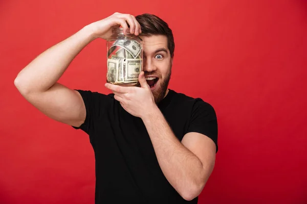 Feliz hombre barbudo sosteniendo tarro lleno de dinero — Foto de Stock