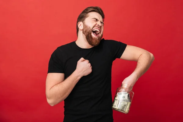 Волнующий бородатый мужчина держит в руках банку, полную денег . — стоковое фото