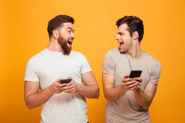 Porträtt av en två lyckliga unga män håller mobiltelefoner — Stockfoto