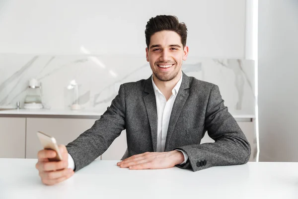 Happy man sitting by the table with smartphone at home — Stock Photo, Image