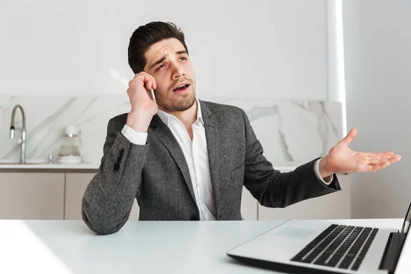 Verward business man zit door de tabel met laptop — Stockfoto