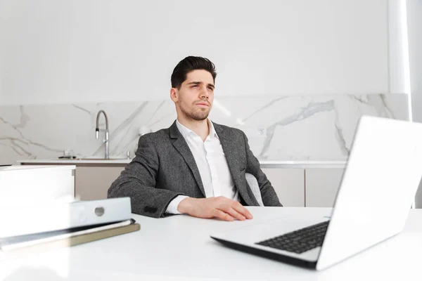 Hombre de negocios serio sentado junto a la mesa con ordenador portátil — Foto de Stock