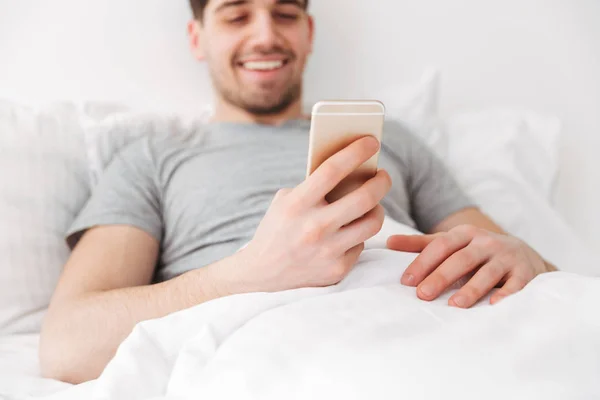 Mutlu esmer adam akıllı telefon kullanırken yatakta yatarken — Stok fotoğraf