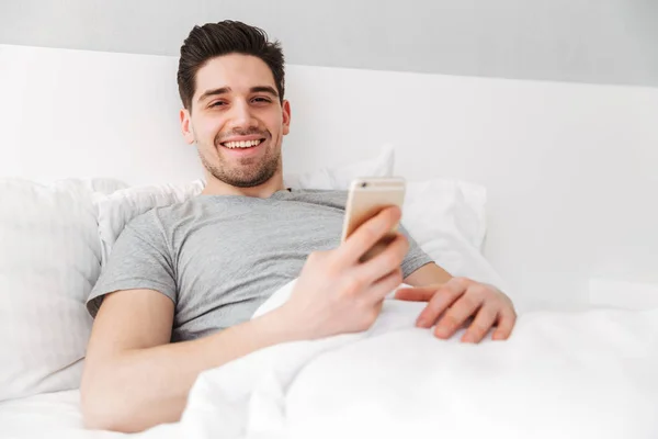 Foto de hombre feliz despierto en camiseta sonriendo mientras yacía solo en —  Fotos de Stock