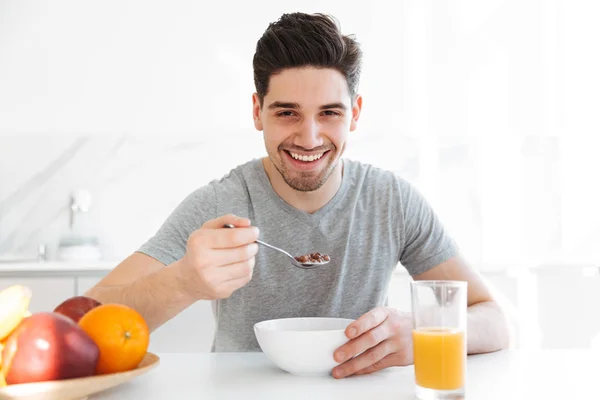 Happy brunette man sitting by the table and eating — Stock Photo, Image