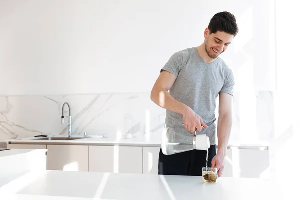Photo of muscular man in casual t-shirt making tea with pouring — Stock Photo, Image