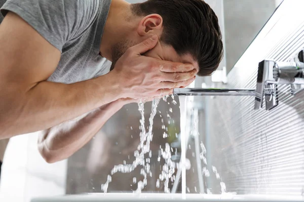 Side view of brunette man washes his in bathroom — Stock Photo, Image