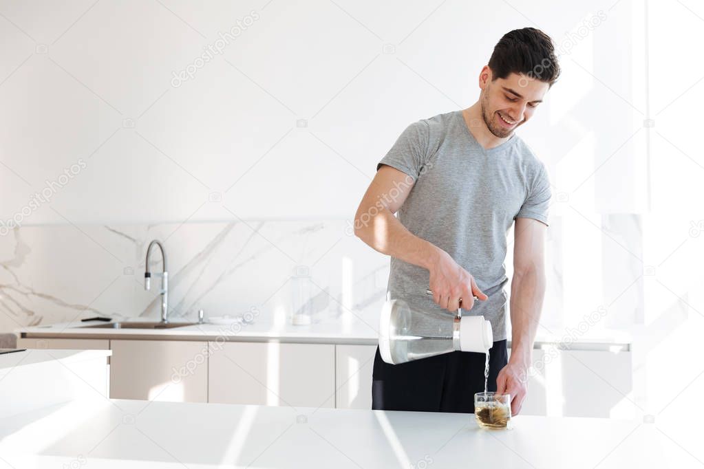 Photo of muscular man in casual t-shirt making tea with pouring 