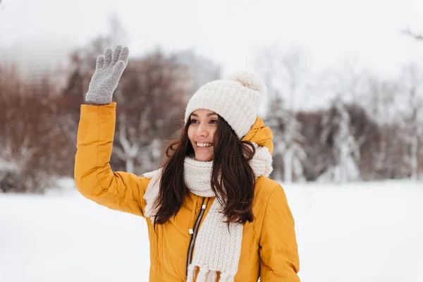 Молодая позитивная женщина машет и здоровается с кем-то в снежном парке — стоковое фото