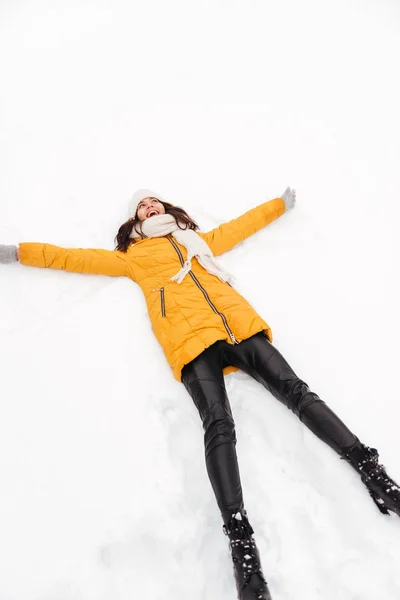Счастливая игривая леди лежит на снегу и делает фигуру снежного ангела — стоковое фото
