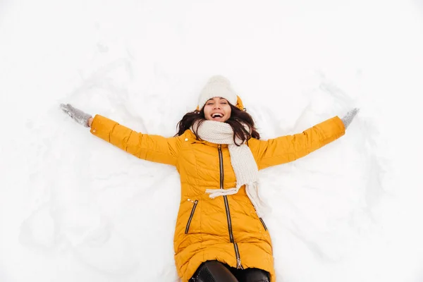 Feliz senhora brincalhão deitado na neve e fazendo figura anjo da neve — Fotografia de Stock