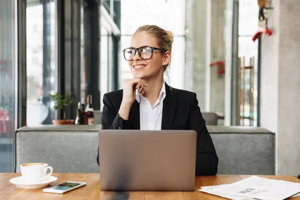 Mujer de negocios sonriente pensativa sentada junto a la mesa en la cafetería — Foto de Stock