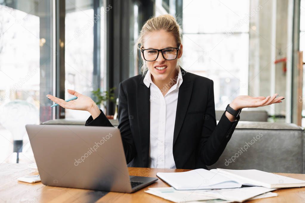 Confused blonde business woman sitting by the table in cafe