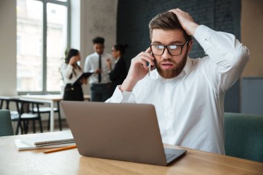 Şok heyecanlı genç beyaz işadamı cep telefonuyla konuşuyor.