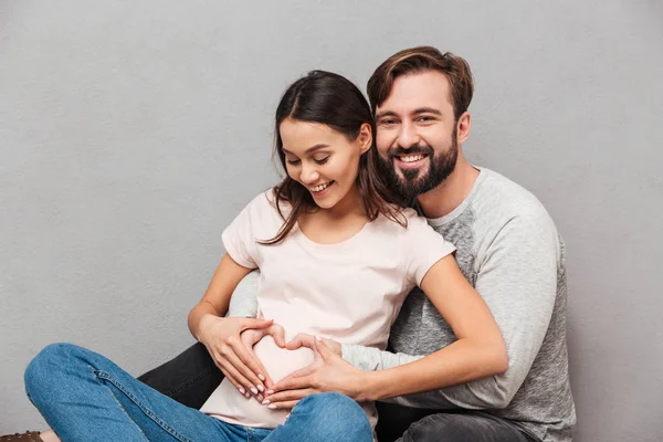 Усміхнений красивий чоловік зі своєю вагітною дружиною робить жест серця . — стокове фото