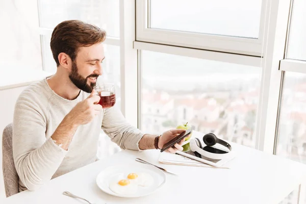 Glad mogen kille dricka te och använda mobiltelefon, medan havi — Stockfoto