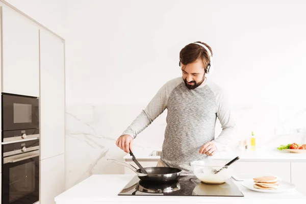 Porträtt av en leende ung man matlagning pannkakor — Stockfoto