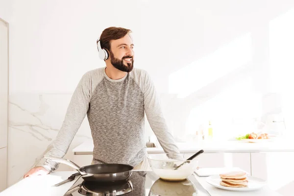 Porträtt av en leende ung man matlagning pannkakor — Stockfoto