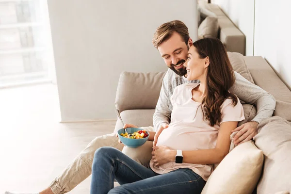 Alegre joven embarazada pareja relajarse en un sofá — Foto de Stock