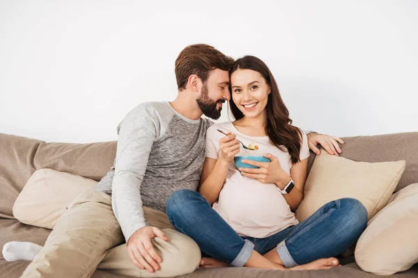 Adorável jovem casal grávida relaxando em um sofá juntos — Fotografia de Stock