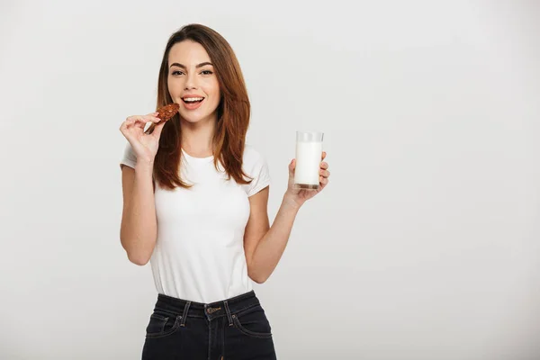 Hübsche junge Frau isst Plätzchen und trinkt Milch. — Stockfoto