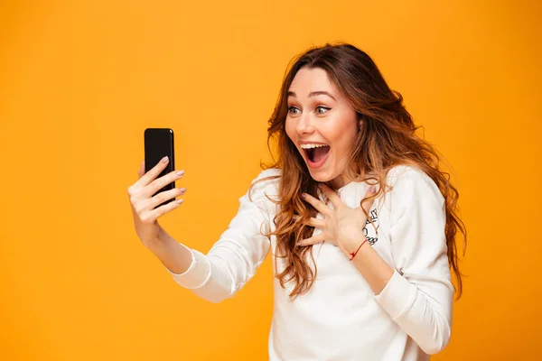 Mulher morena surpreso em suéter usando smartphone enquanto se alegra — Fotografia de Stock