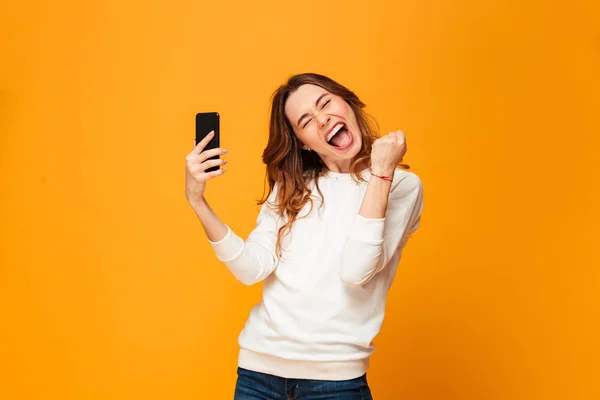Feliz gritando morena mujer en suéter celebración de teléfono inteligente — Foto de Stock