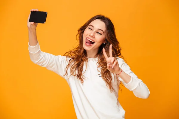 Emotional young woman make selfie by mobile phone with peace gesture. — Stock Photo, Image