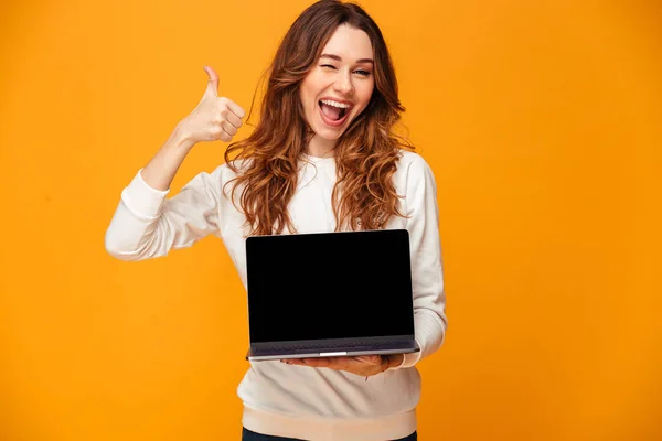 Mulher morena alegre em suéter mostrando tela do computador portátil em branco — Fotografia de Stock