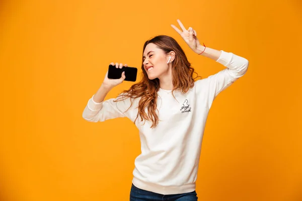 Emotionale junge Frau hört Musik mit dem Handy tanzen. — Stockfoto