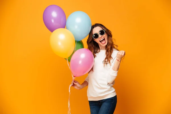 Felice urlando donna bruna in maglione e occhiali da sole in possesso di palloncini — Foto Stock