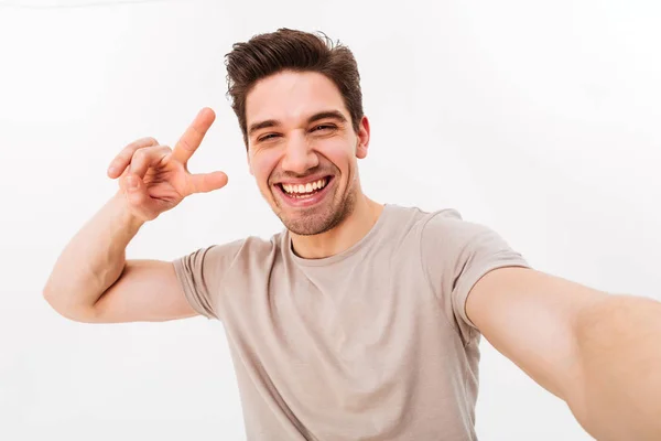 Sorrindo cara com cabelo castanho mostrando sinal de paz na câmera enquanto p — Fotografia de Stock