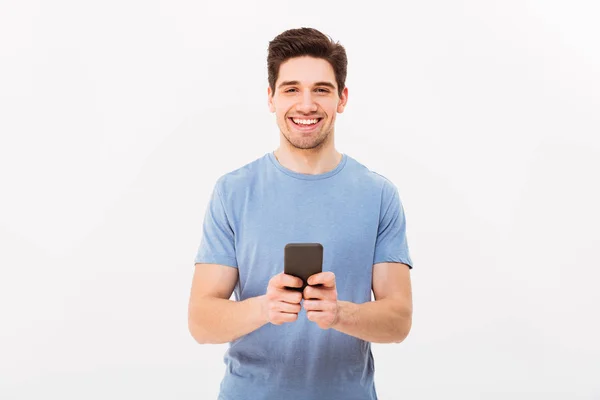 Gelukkig man 30s in casual t-shirt typen van sms of surfen op internet — Stockfoto