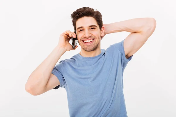 Hombre sonriente en camiseta hablando por teléfono inteligente mientras sostiene la cabeza — Foto de Stock