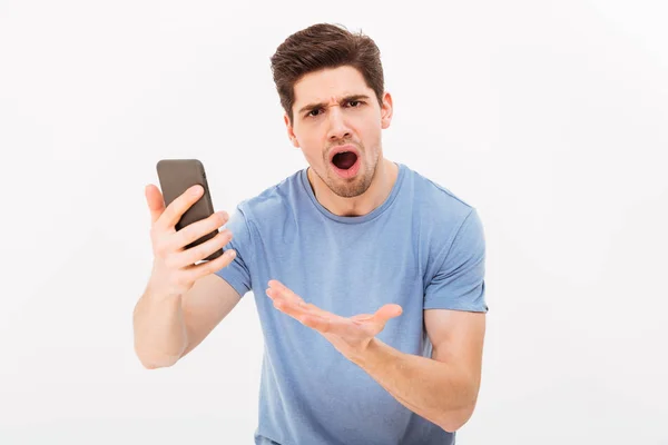 Picture of frustrated unshaved man in casual t-shirt holding sma — Stock Photo, Image