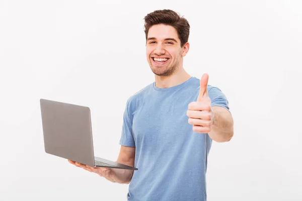 Foto av leende man i casual t-shirt holding silver laptop och — Stockfoto