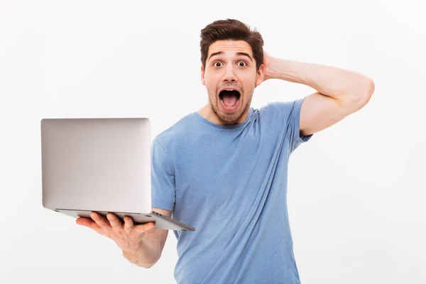 Bilde av en kjekk mann i en tilfeldig t-skjorte som holder en sølvbærbar laptop – stockfoto